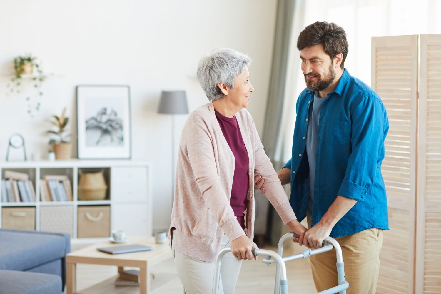 Stock image of a young man helping an older woman with a walker